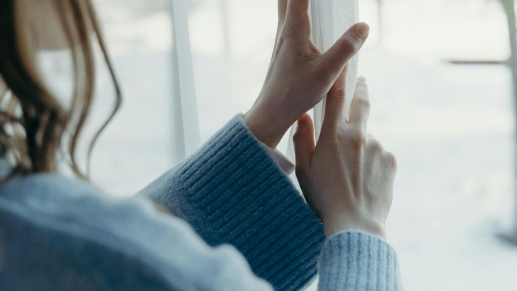 Woman embracing daily wellness habits by opening curtains to sunlight, symbolizing emotional healing and growth through self-care.
