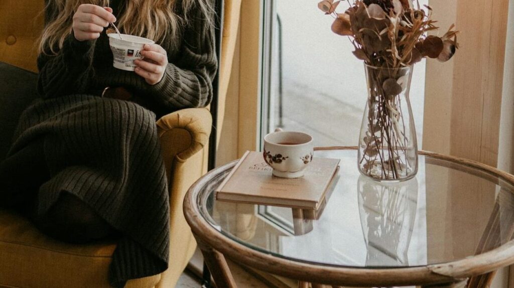 Woman sitting in a cozy armchair by a window, surrounded by houseplants, enjoying a quiet moment indoors.