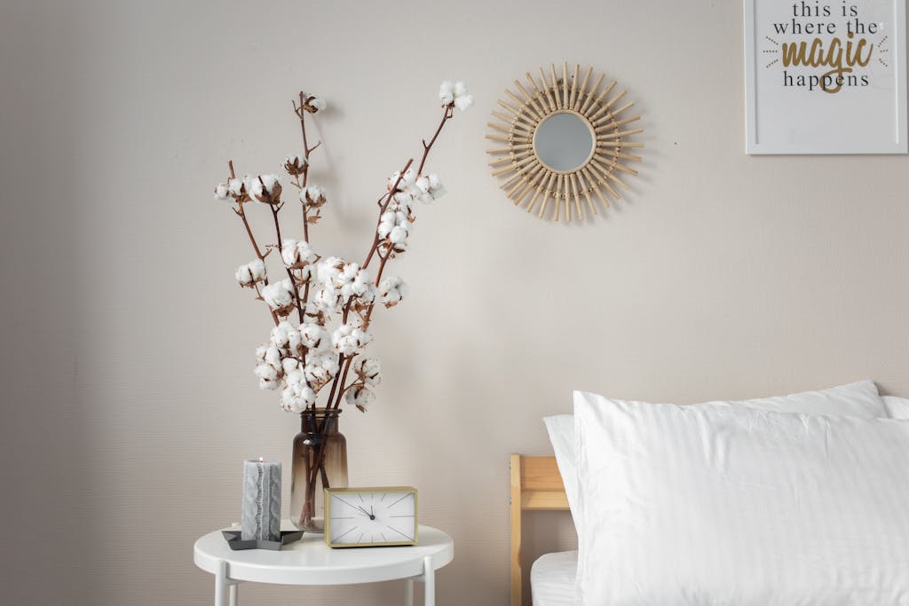 A calming bedroom scene, minimalist bedside table with cotton flowers, candle, table clock and modern decor details like a mirror and wall art — calm home decor for peaceful mornings.