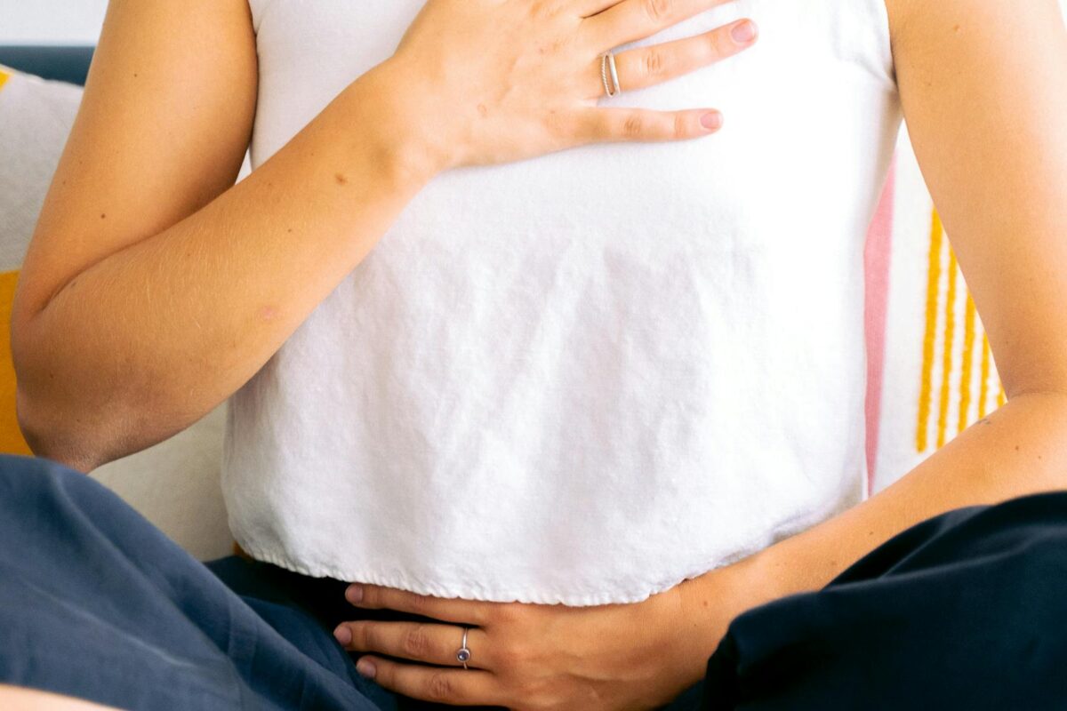 Woman sitting cross-legged in meditation, hands on chest and belly, focusing on breathing and relaxation.