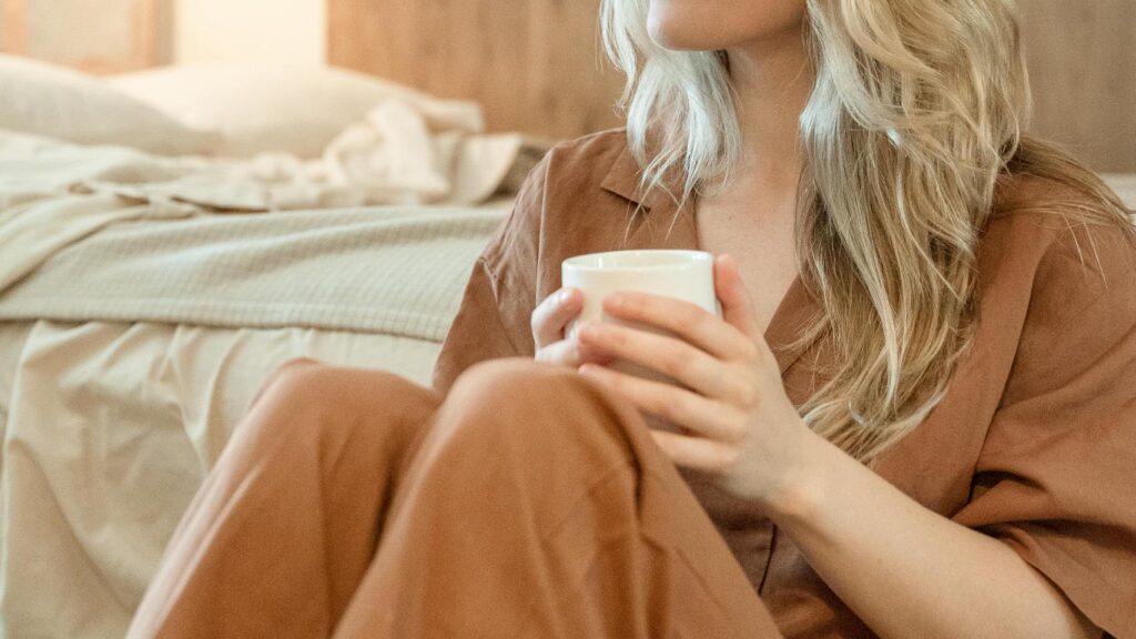 Woman practicing self-care with simple self-care habits, holding a warm cup in her bedroom during her emotional healing journey.