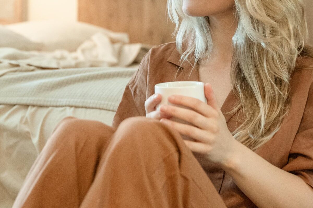 Woman practicing self-care with simple self-care habits, holding a warm cup in her bedroom during her emotional healing journey.