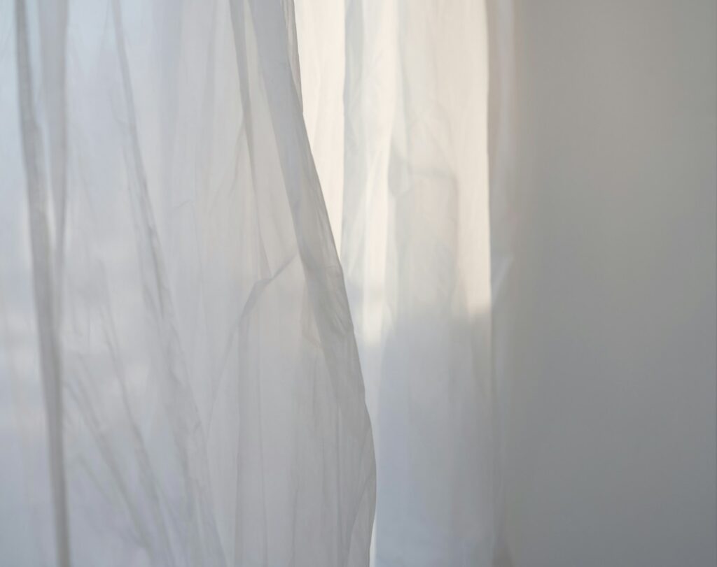 Sheer curtains moving gently in an open window, catching shifting light