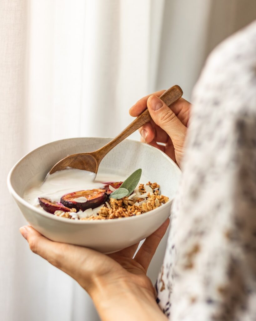 Close-up of hands holding a nourishing bowl of yogurt, oats, and fresh produce, capturing a moment of grounding nutrition habits.