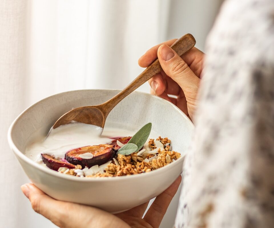 Close-up of hands holding a nourishing bowl of yogurt, oats, and fresh produce, capturing a moment of grounding nutrition habits.