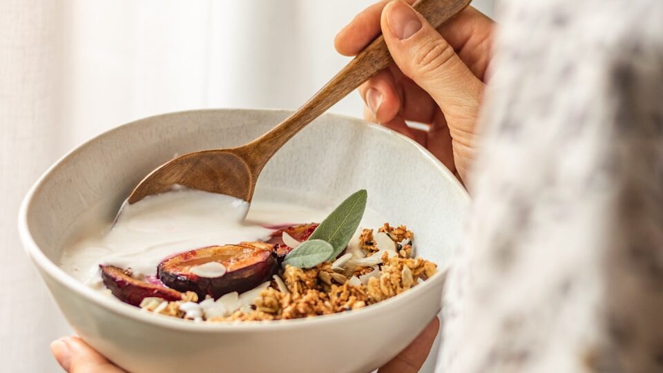 Close-up of hands holding a nourishing bowl of yogurt, oats, and fresh produce, capturing a moment of grounding nutrition habits.