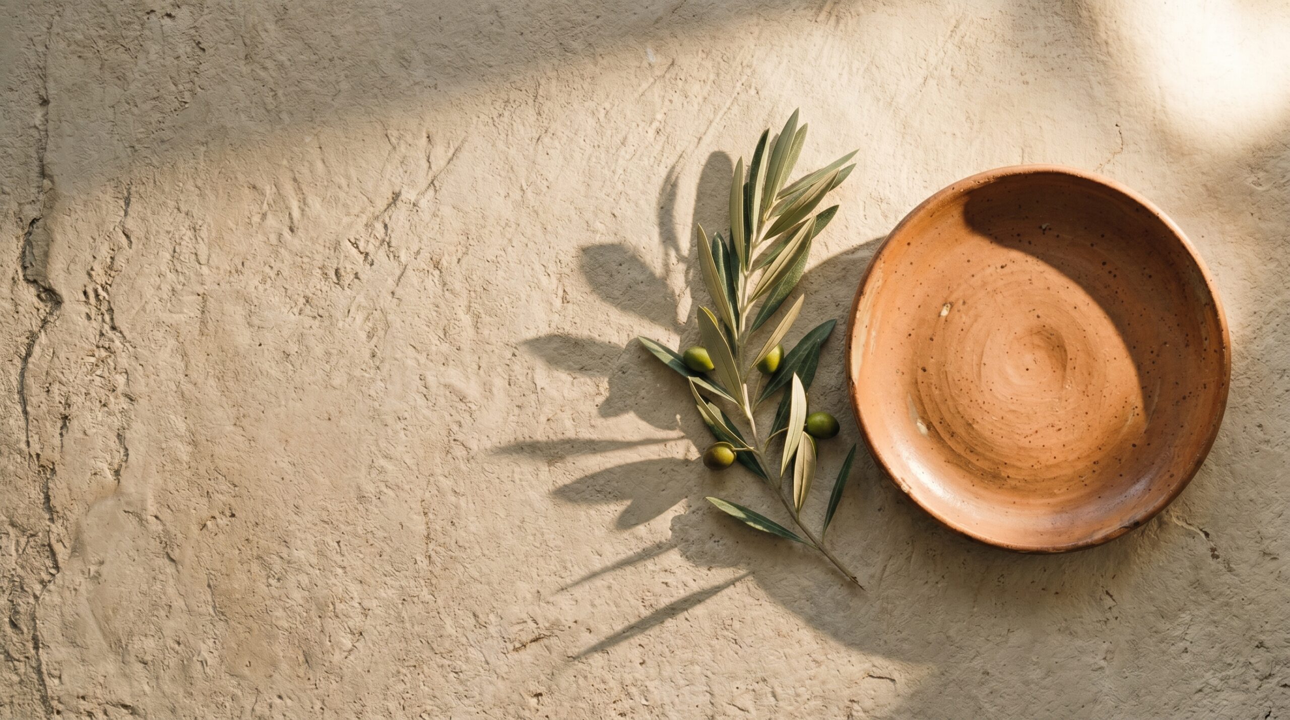 A leaf and wooden plate on a soft cream linen with sunlight representing warmth, refuge, and home.
